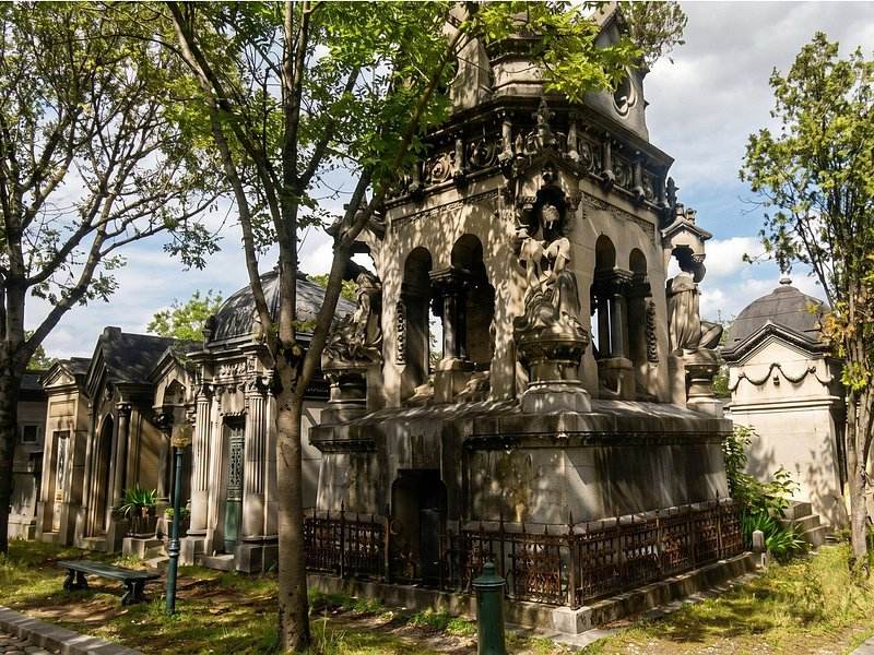 A carved stone monument among the trees of Montmartre Cemetery